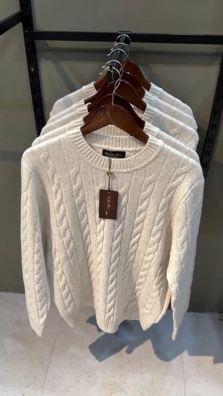 Cream cable-knit sweaters hanging on wooden hangers on a black clothing rack.