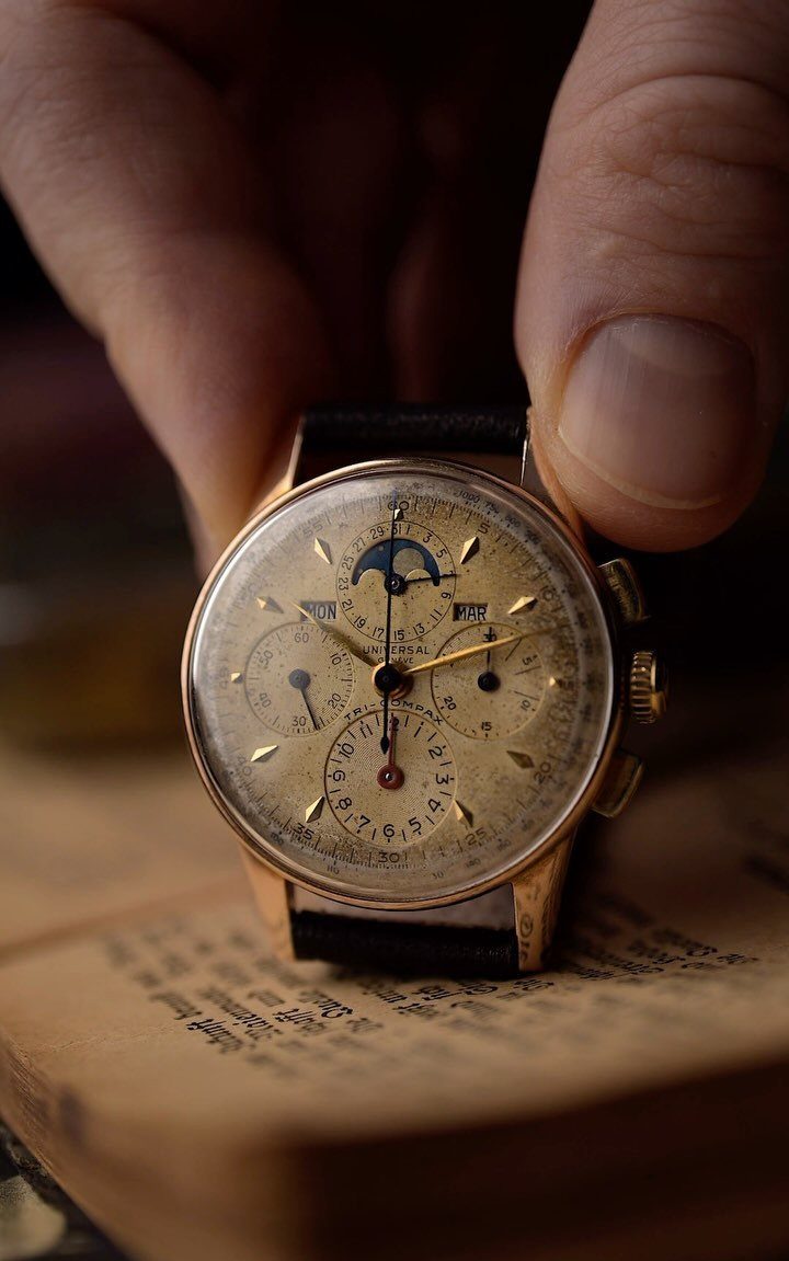 A hand holding a vintage gold mechanical wristwatch over an open antique book.