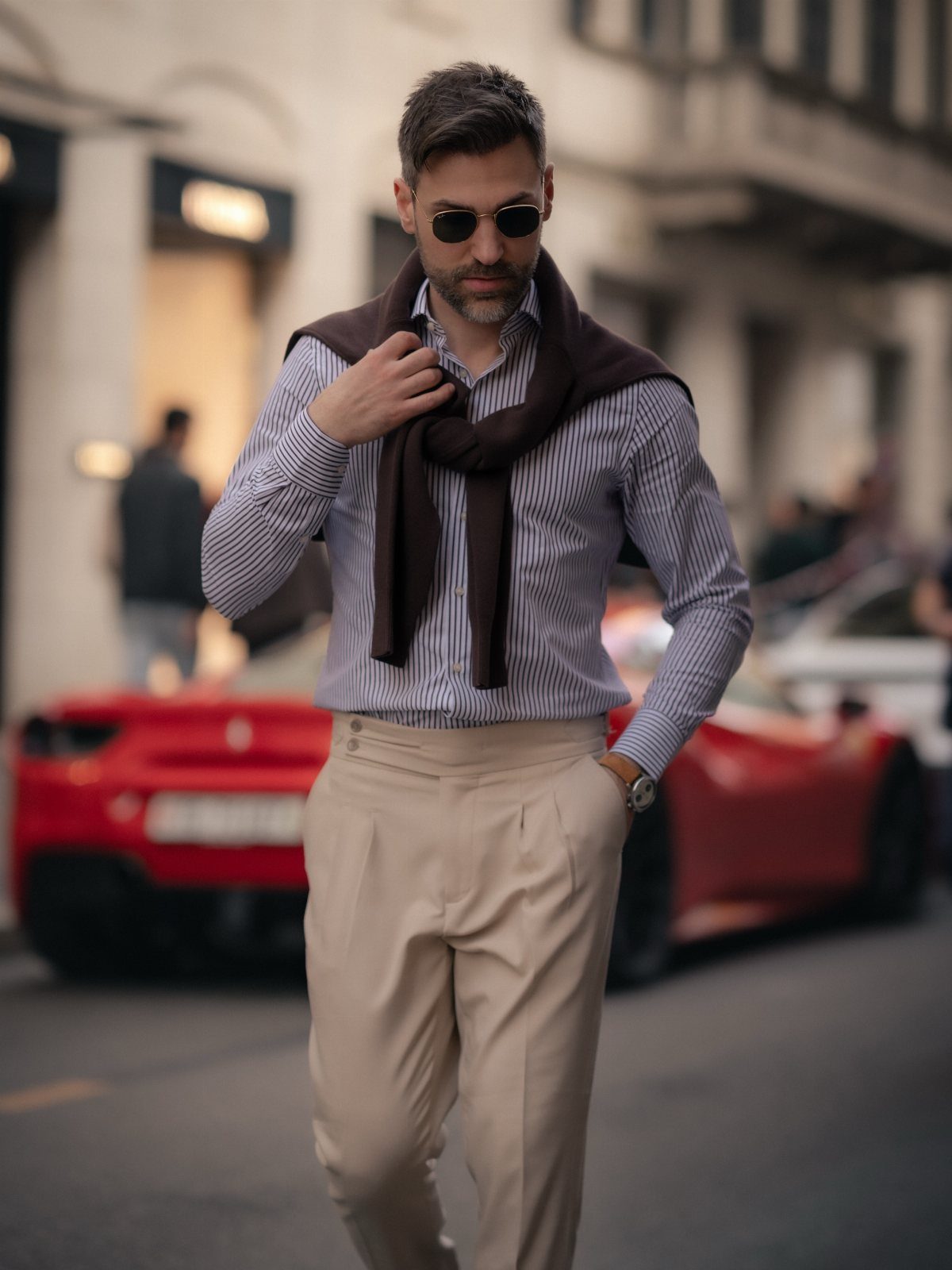 A man in a striped dress shirt and cream trousers walking through a city street.