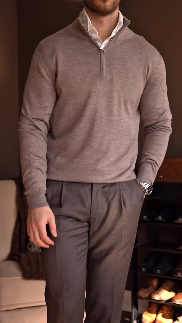 Man wearing a taupe quarter-zip sweater over a white collared shirt and grey trousers.