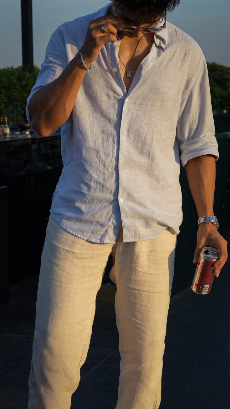 Man in a light blue linen shirt and cream linen trousers standing outdoors at sunset.