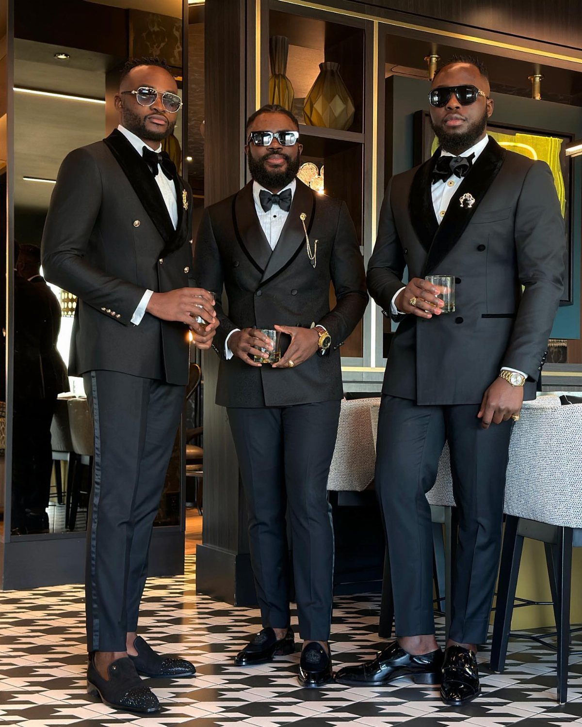 Three men posing in elegant black velvet lapel tuxedos and bow ties in a lounge.