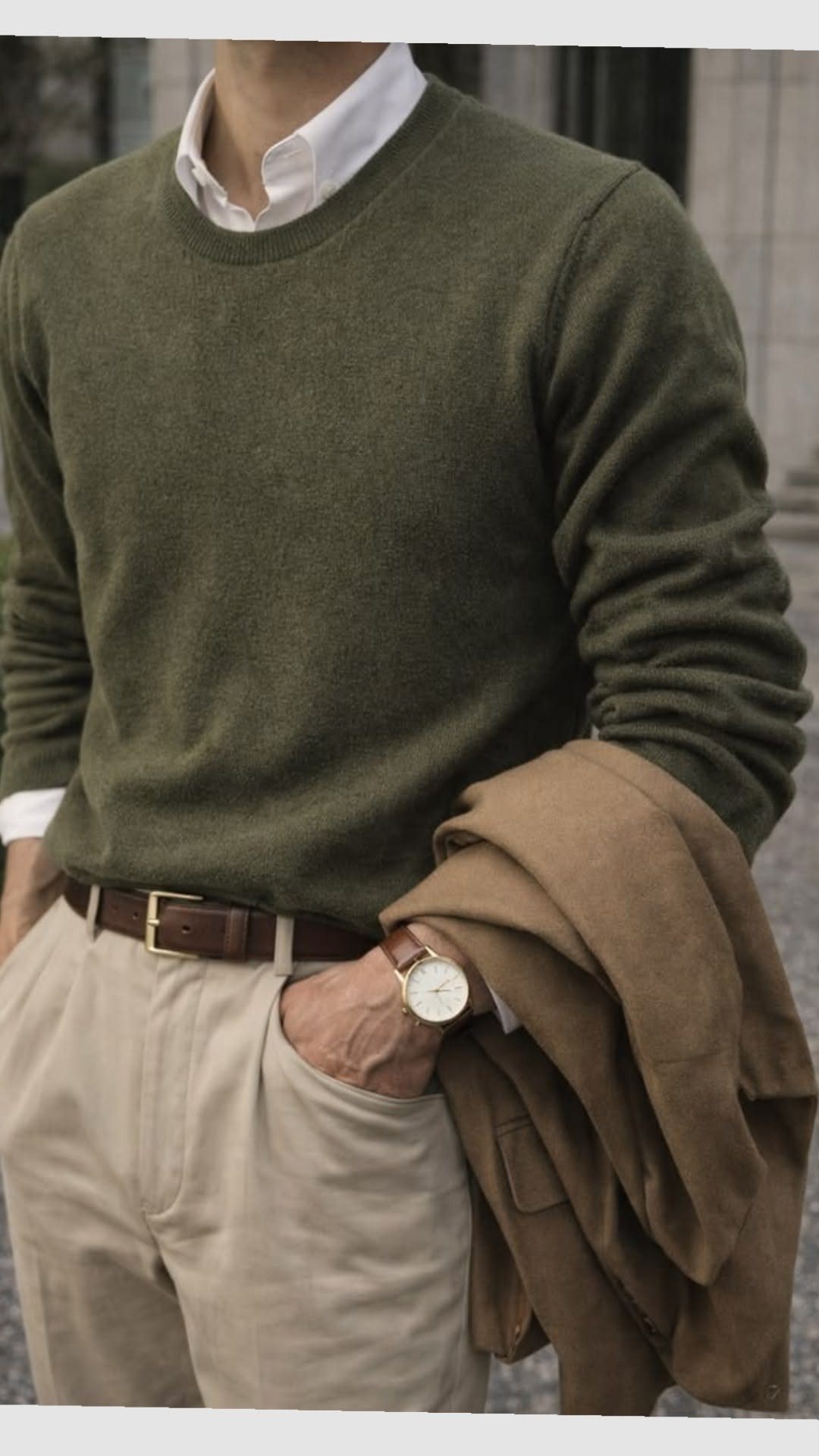 Man wearing an olive green sweater, white collared shirt, and beige trousers with a brown belt.