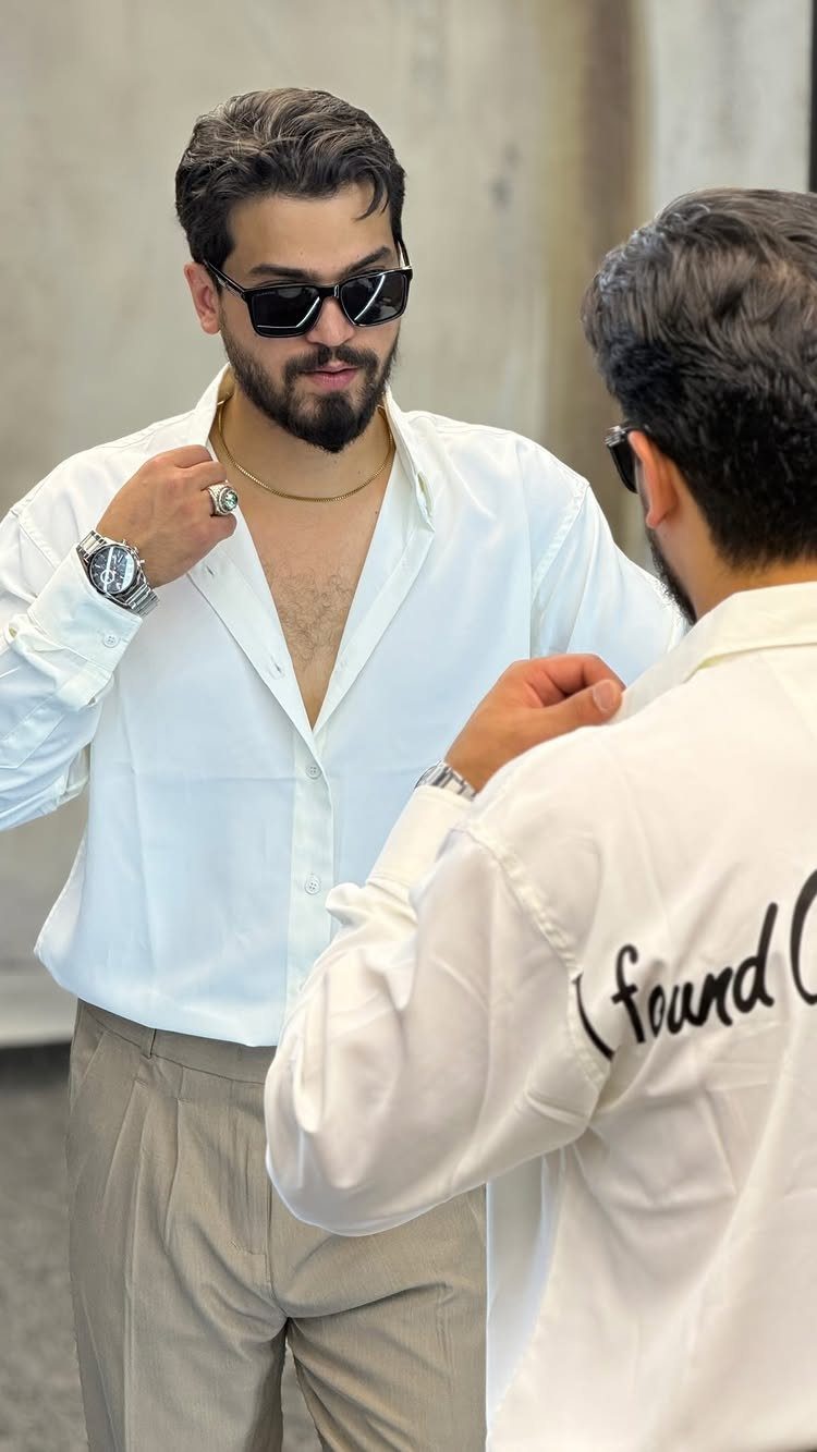 Man wearing a white button-down shirt and beige pleated chinos with sunglasses.