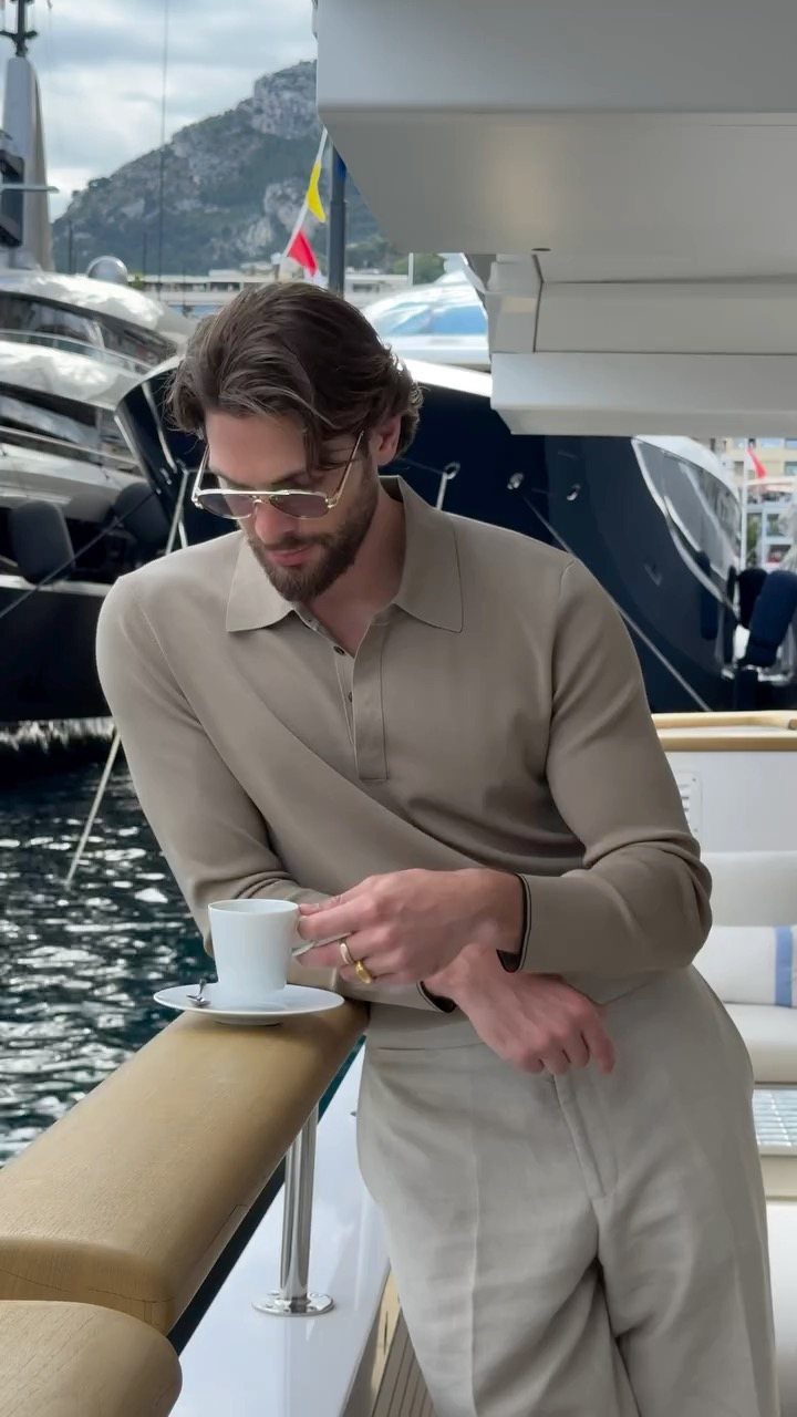 Man in a beige long-sleeved polo shirt and trousers leaning on a boat railing.