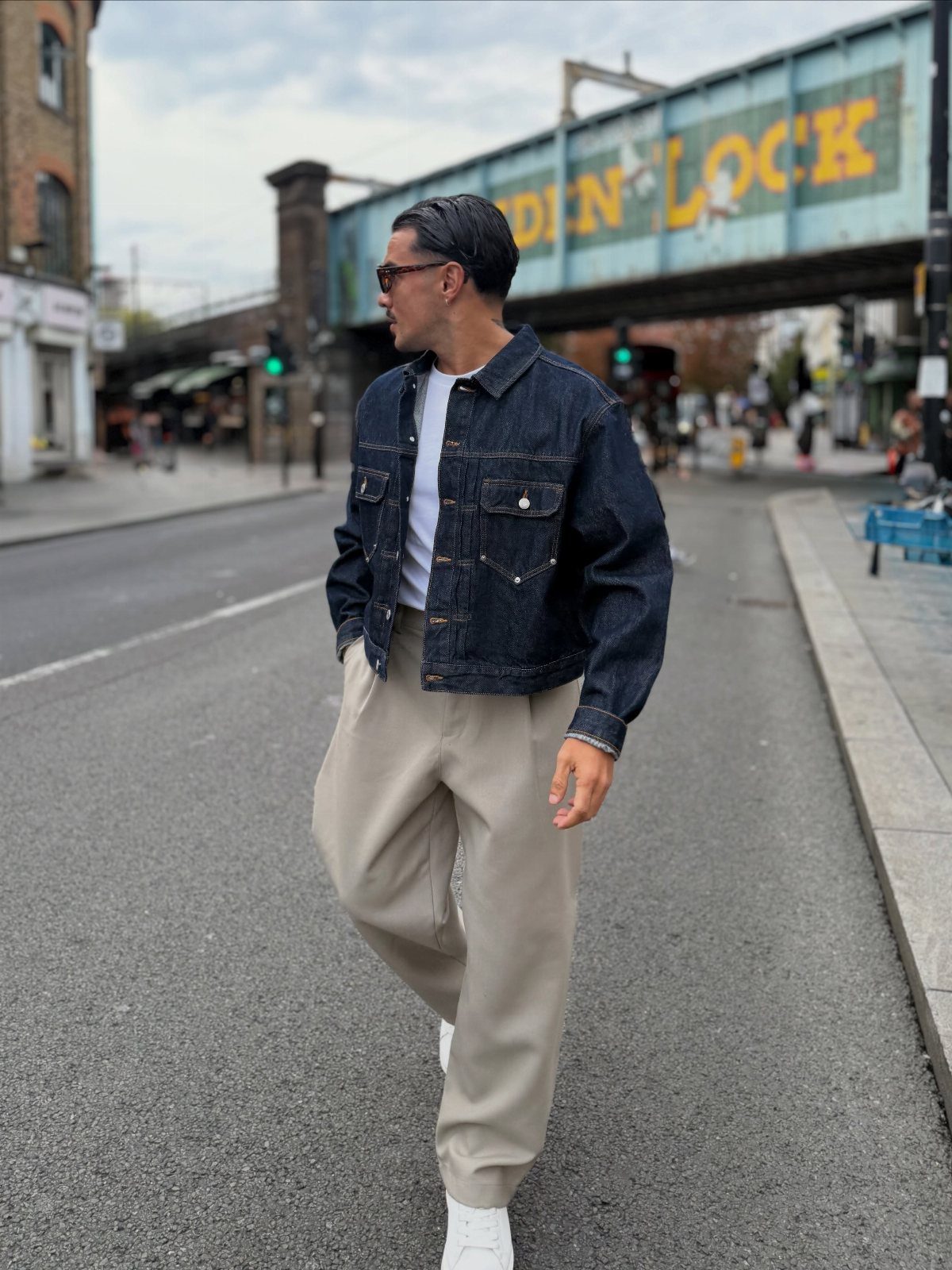 Man walking down a city street wearing a denim jacket and white t-shirt.
