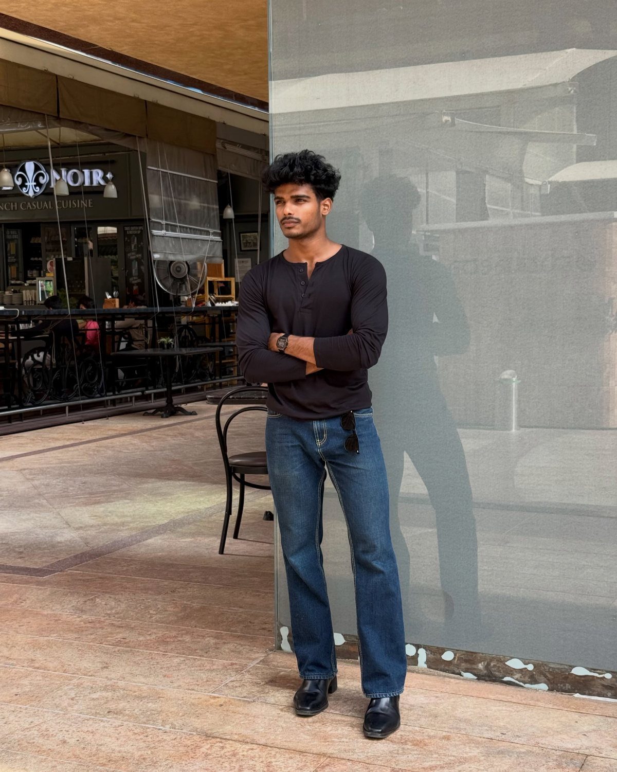 Man wearing a black long-sleeved Henley shirt and blue denim jeans standing outdoors.