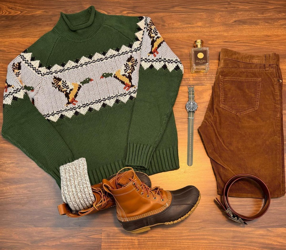 Green duck pattern sweater, brown corduroy pants, and tan duck boots laid on wood.