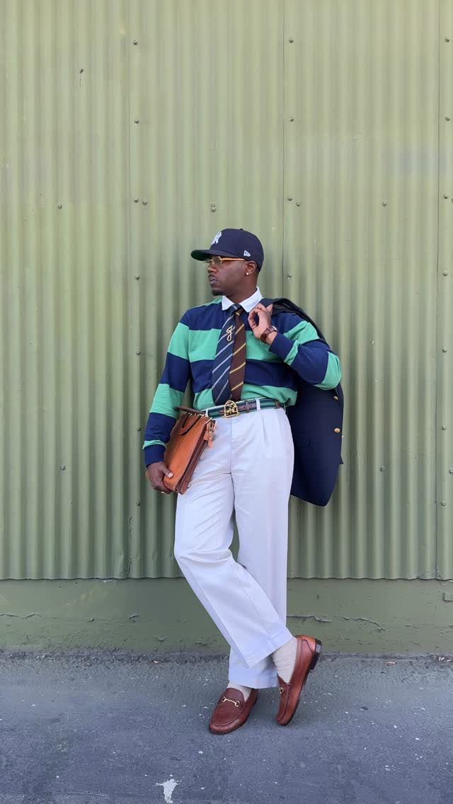 Man in a navy and green striped rugby shirt, white trousers, and brown loafers posing outdoors.