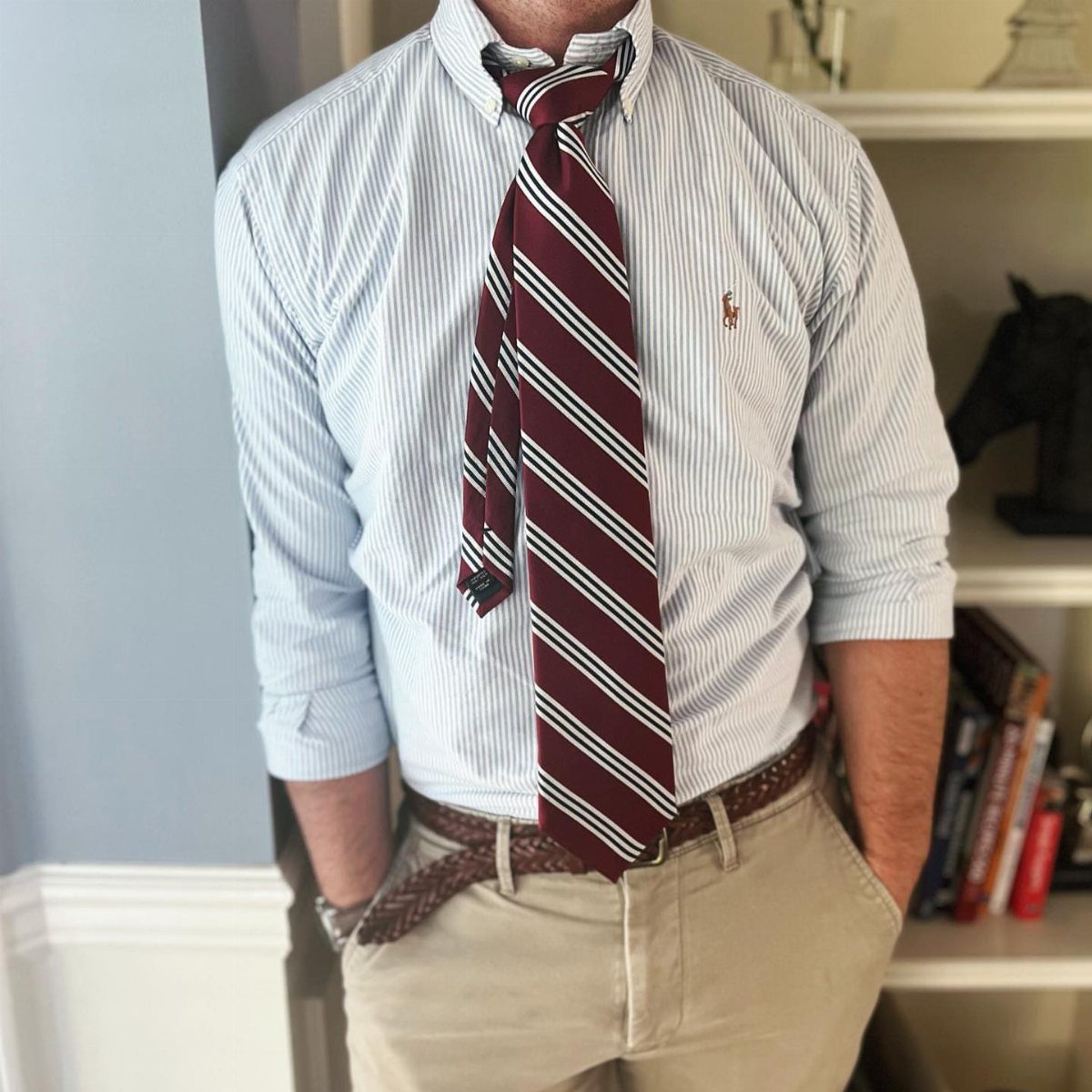 Man wearing a striped button-down shirt, a maroon striped tie, and khaki pants.