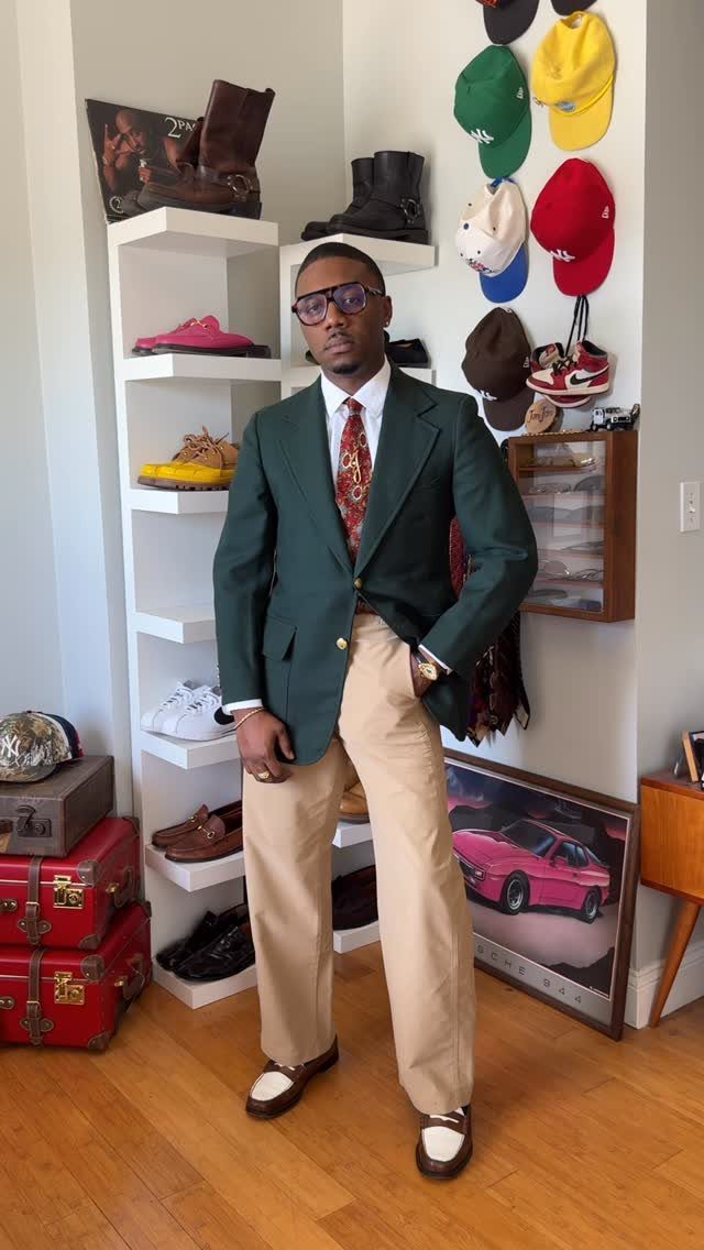 Man wearing a green blazer, white shirt, red tie, and tan khaki pants standing indoors.