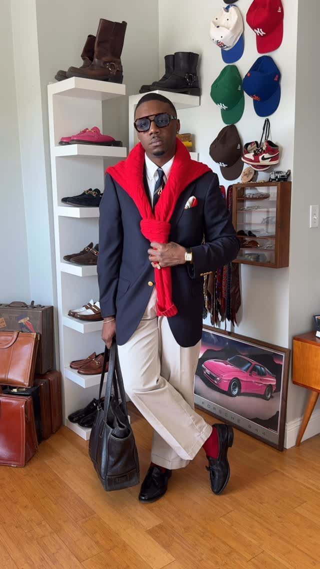 Man wearing a navy blazer, white shirt, tie, and cream chinos standing in a room.