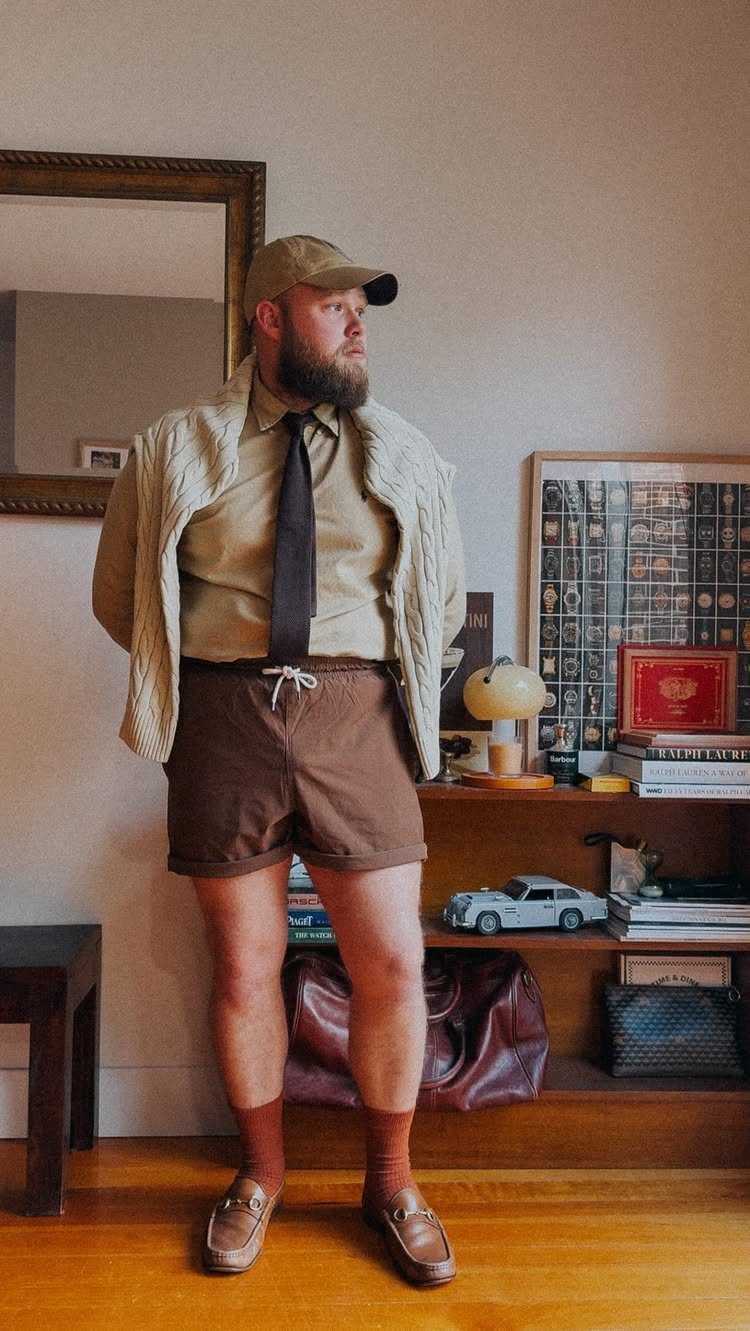 A man in preppy attire wearing brown leather loafers and brown socks standing indoors.