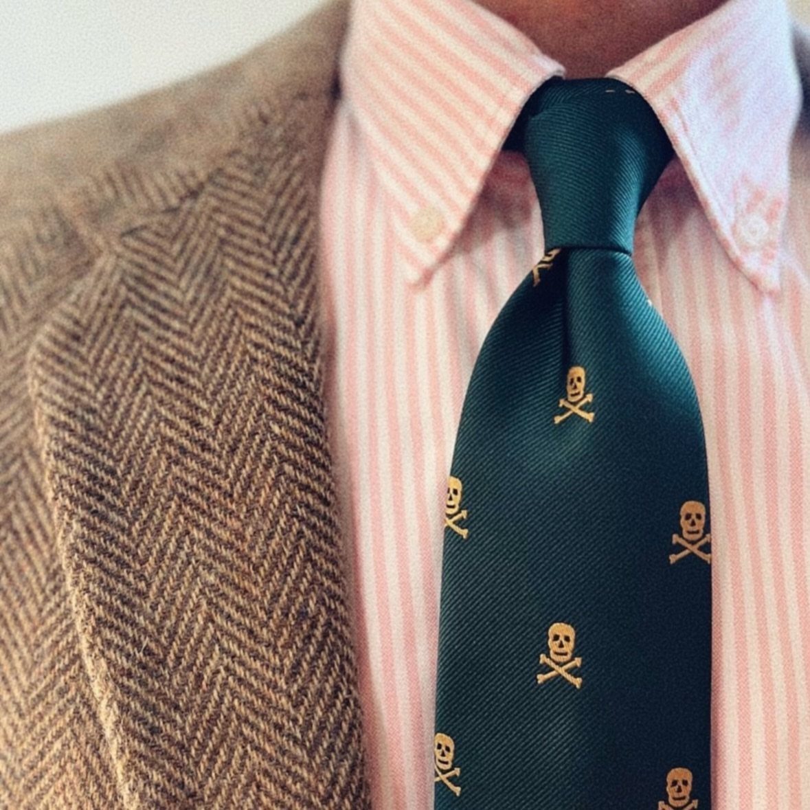 Man wearing a pink striped shirt, green skull pattern tie, and herringbone tweed blazer.