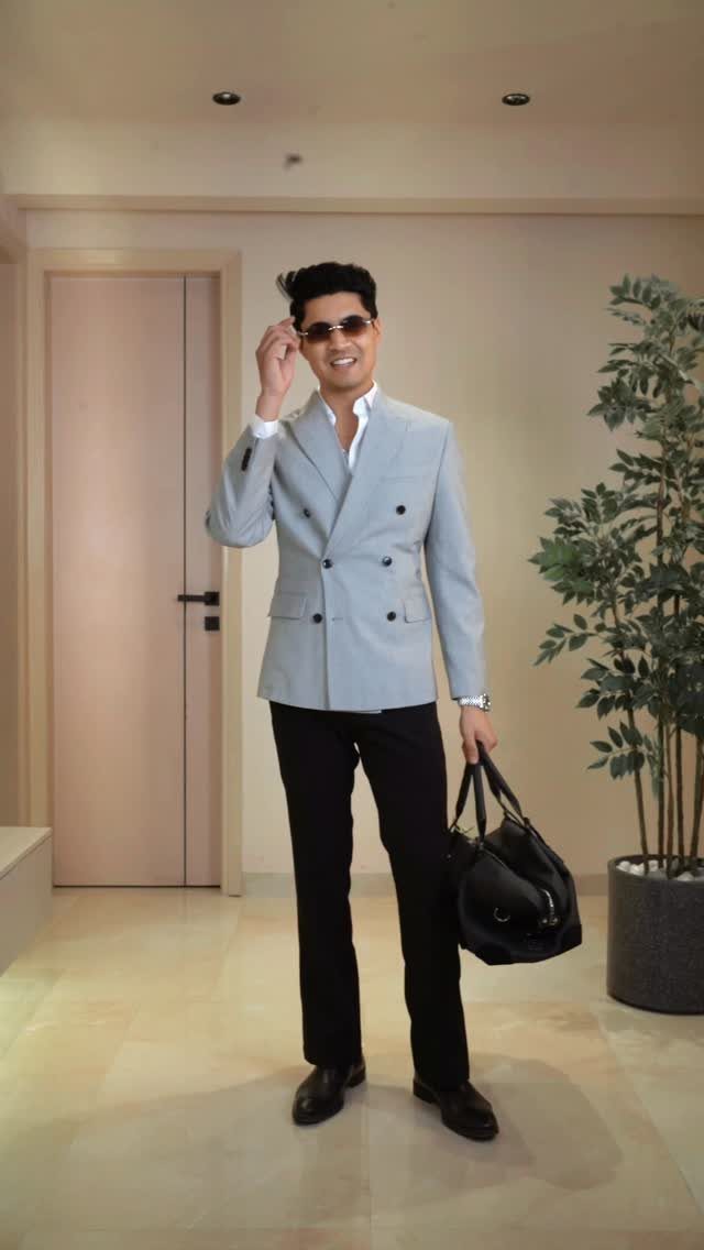 A man posing in a light grey double-breasted blazer, white shirt, and black trousers.