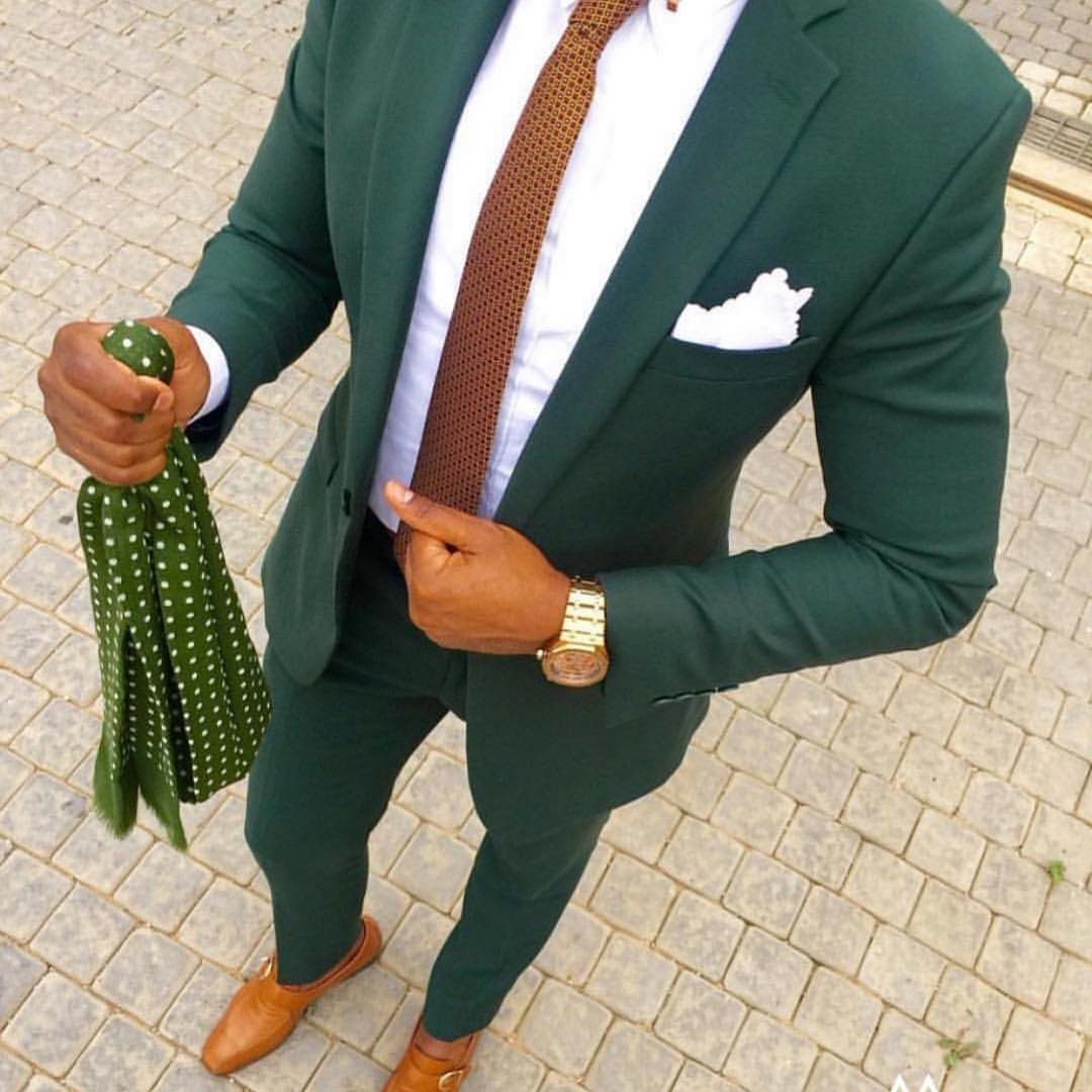 Man standing in a slim-fit hunter green suit with a brown tie and tan loafers.