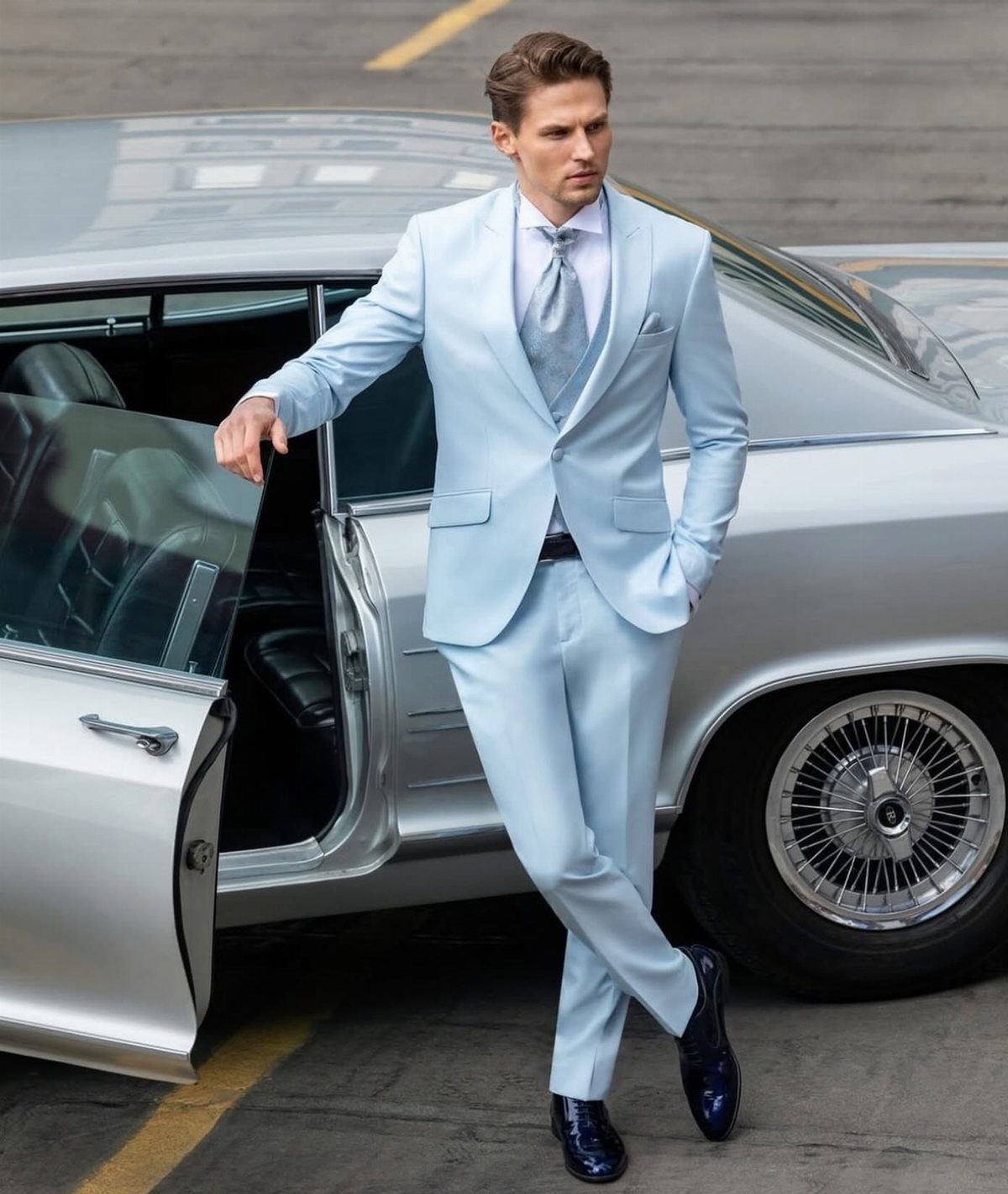 A man in a light blue suit posing next to a silver vintage car.