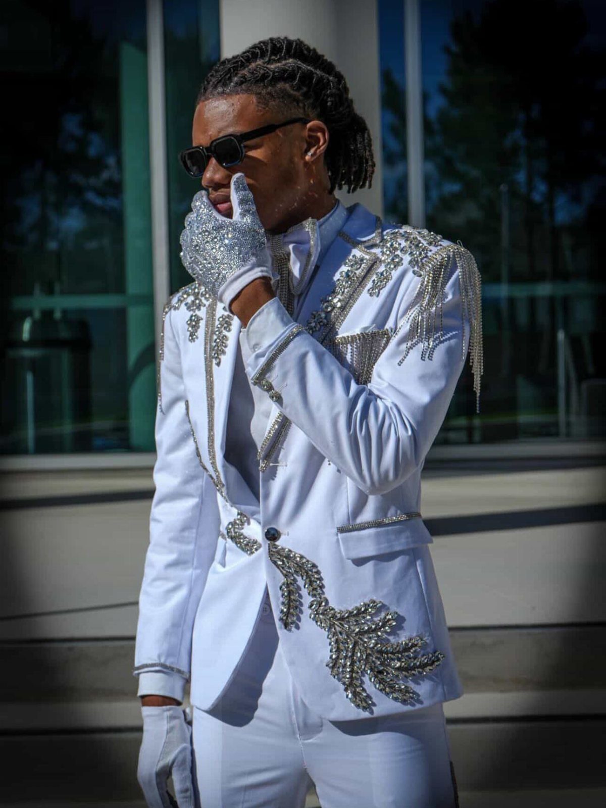 A man in a white suit decorated with silver sequins and fringe posing outdoors.