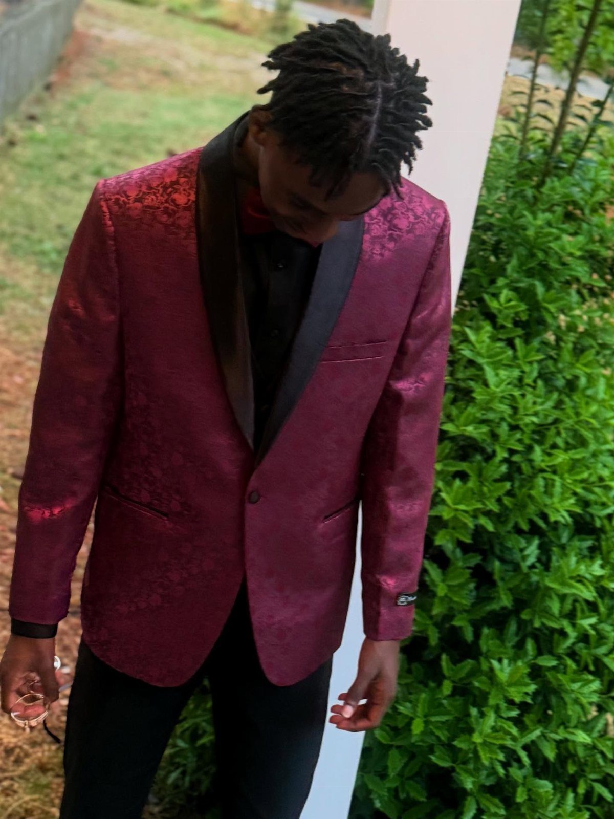 A man wearing a burgundy patterned blazer with black lapels and black trousers.