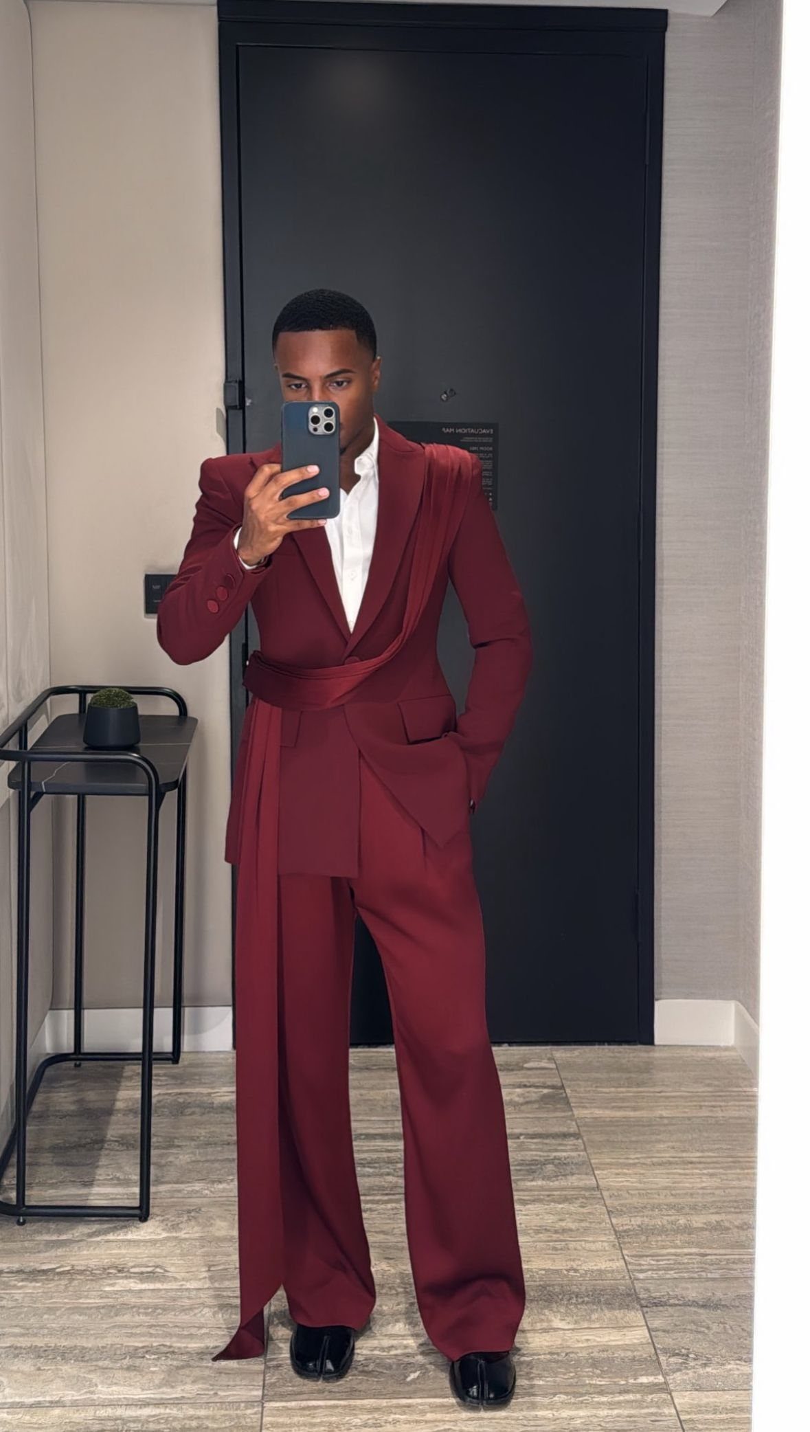 Man in a burgundy tailored blazer with a draped waist and matching trousers posing for a selfie.