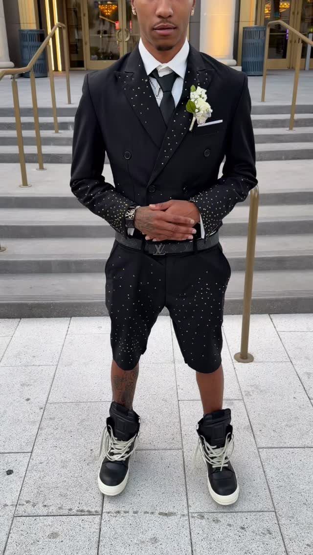 Man wearing a black patterned blazer, matching shorts, white shirt, and black sneakers.