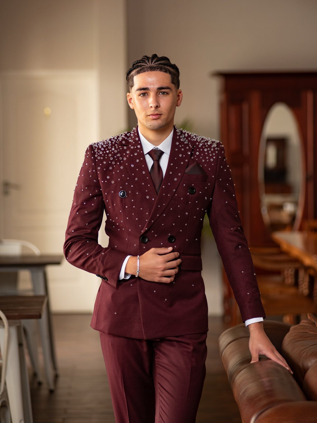 A young man posing in a burgundy rhinestone-embellished suit with a matching tie.
