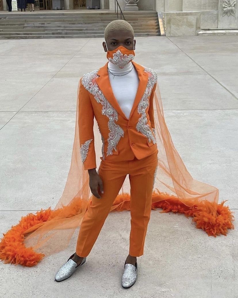 A person in an orange embroidered suit with a long orange tulle cape and silver shoes.