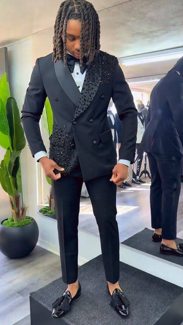 A young man posing in a black sequined double-breasted suit and tassel loafers.