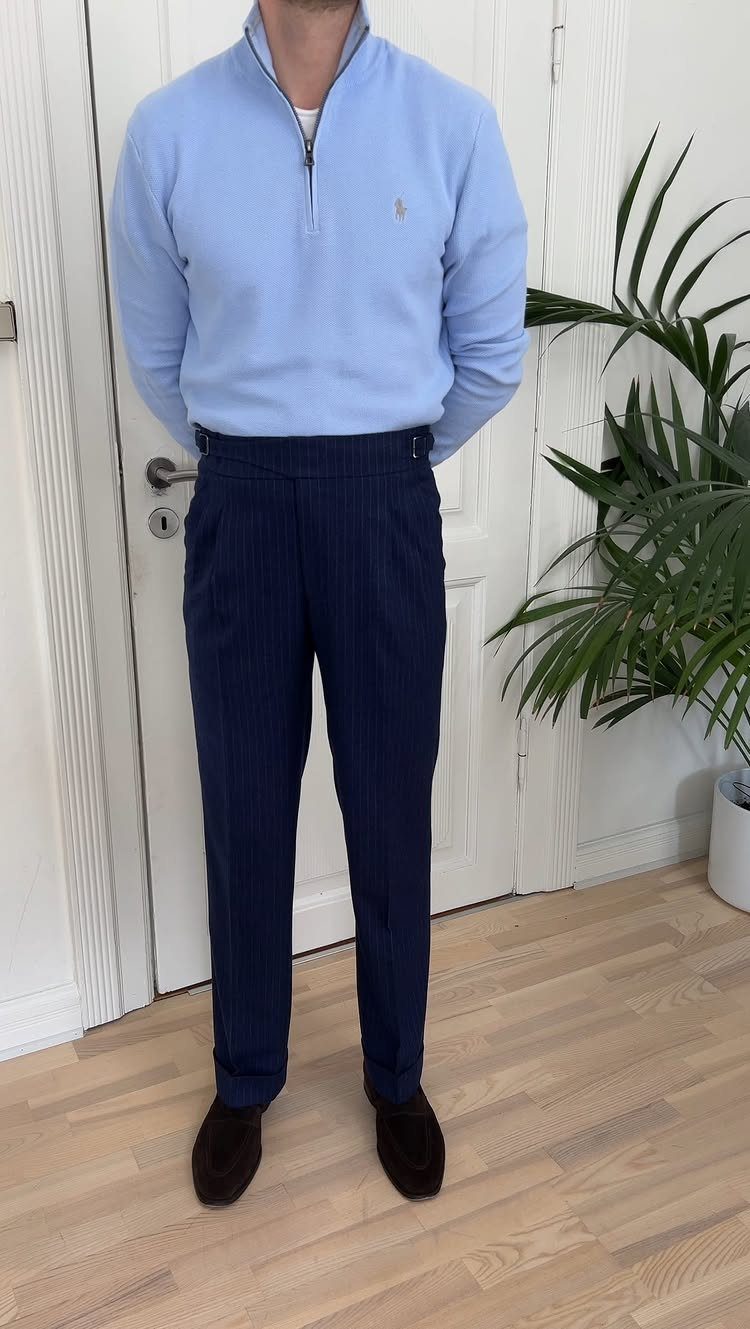 Man wearing a light blue pullover and navy blue pinstriped semi-formal trousers.