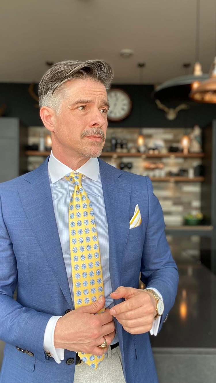 Man wearing a blue blazer over a light blue shirt and a yellow patterned tie.