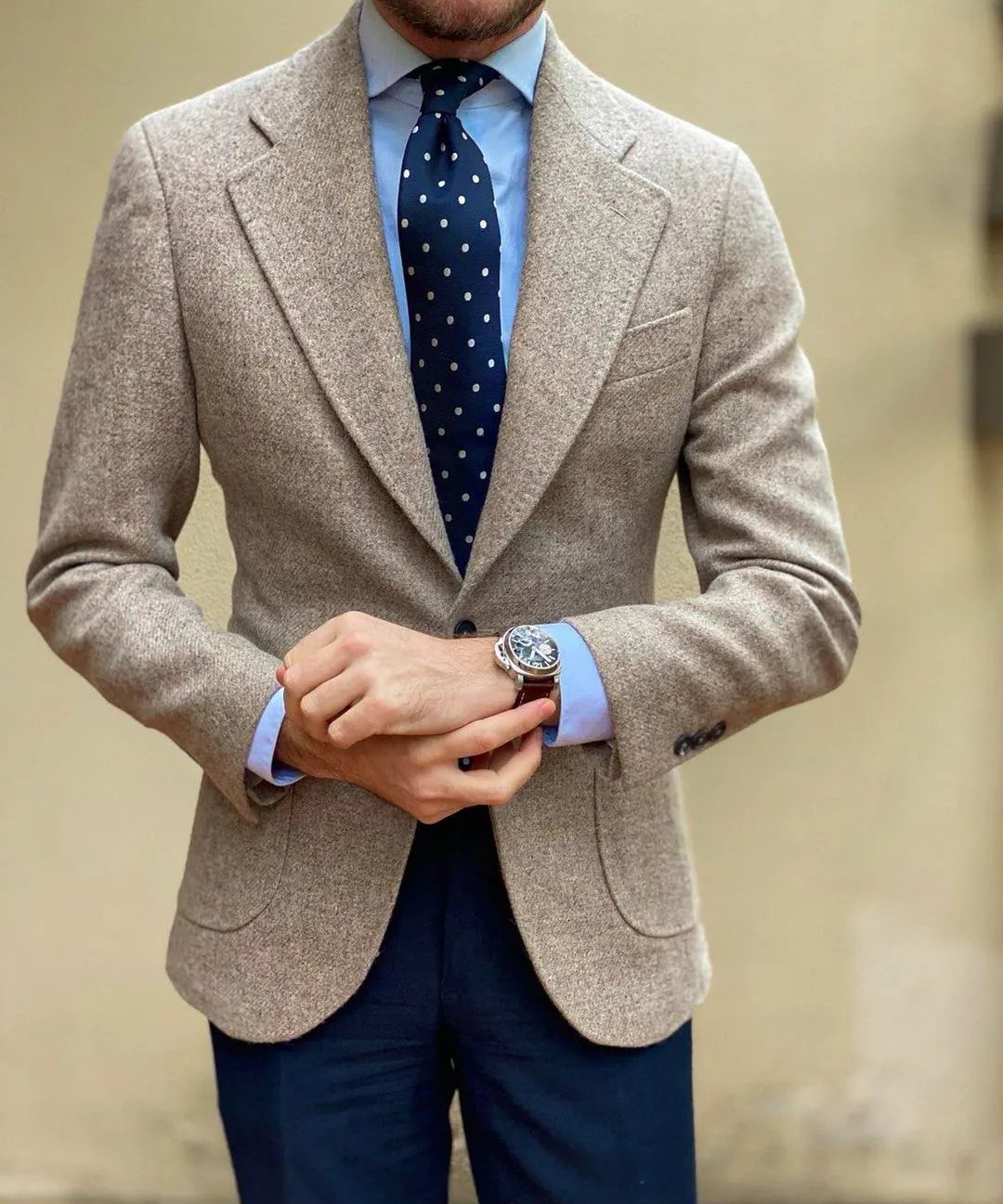 Man wearing a slim-fit beige textured blazer, light blue shirt, and navy polka-dot tie.