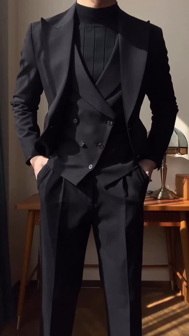 Man wearing a black slim-fit three-piece suit and a black turtleneck sweater indoors.