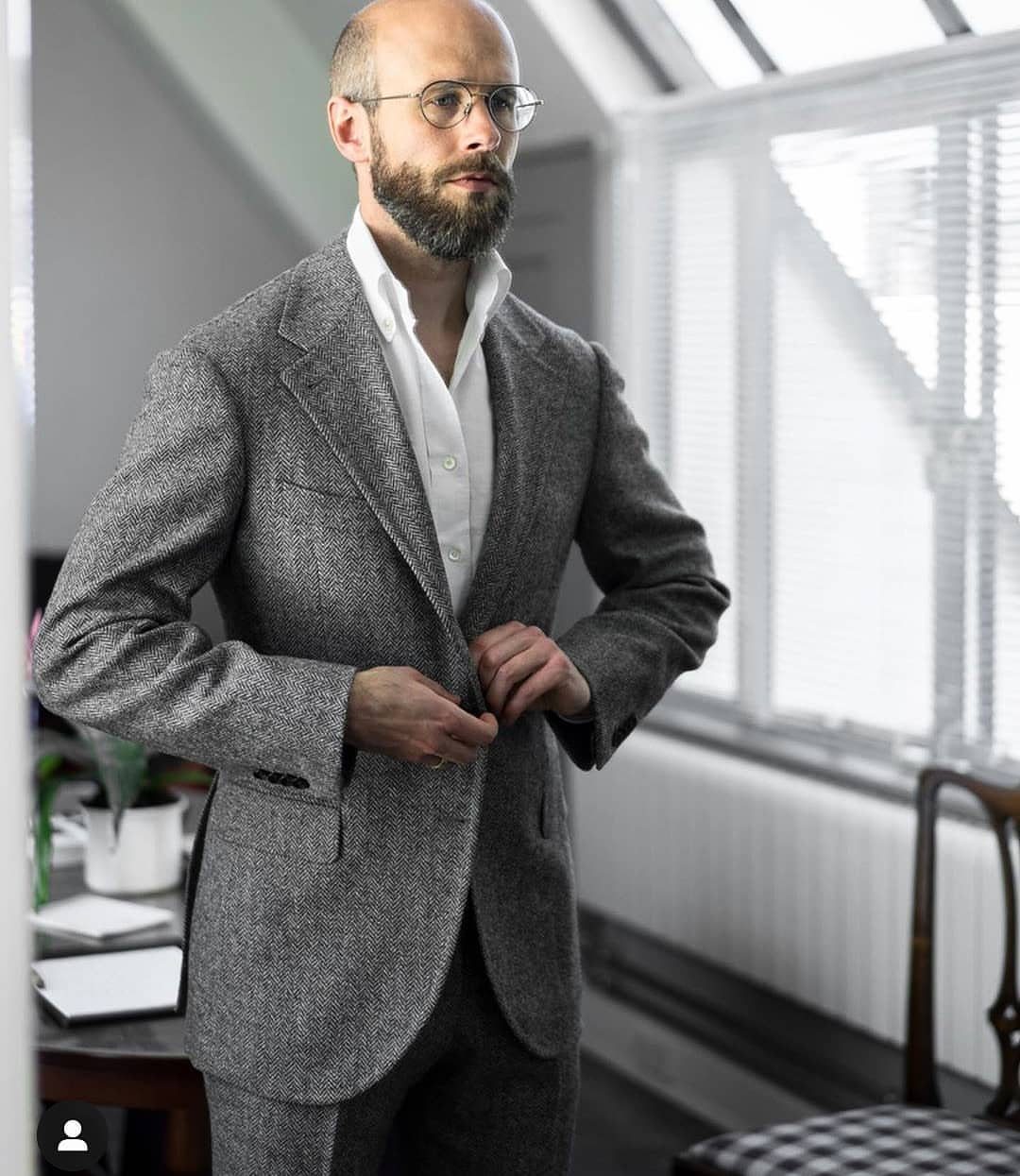 Man wearing a grey herringbone patterned sport coat and white shirt standing by a window.