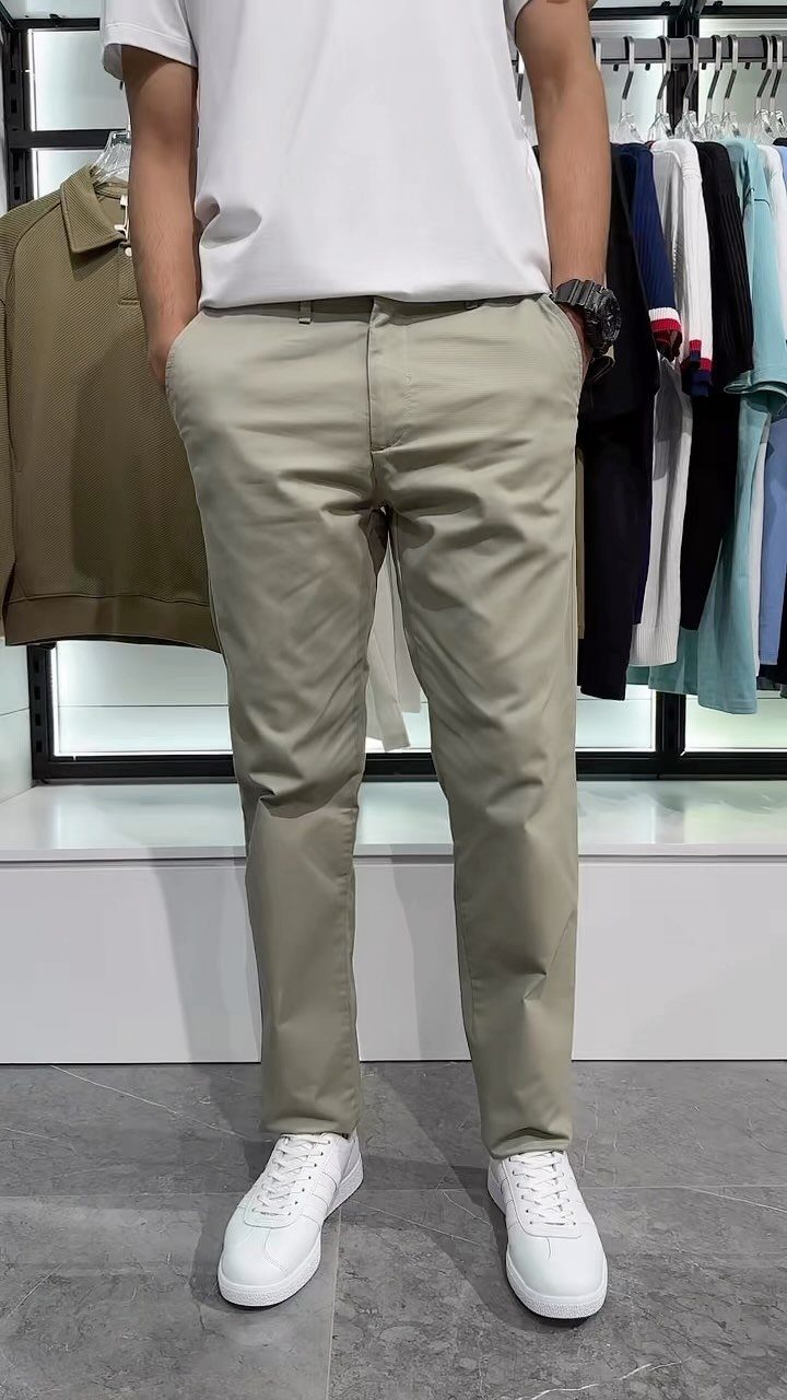 Man wearing a white t-shirt, beige chinos, and white sneakers standing in a clothing store.