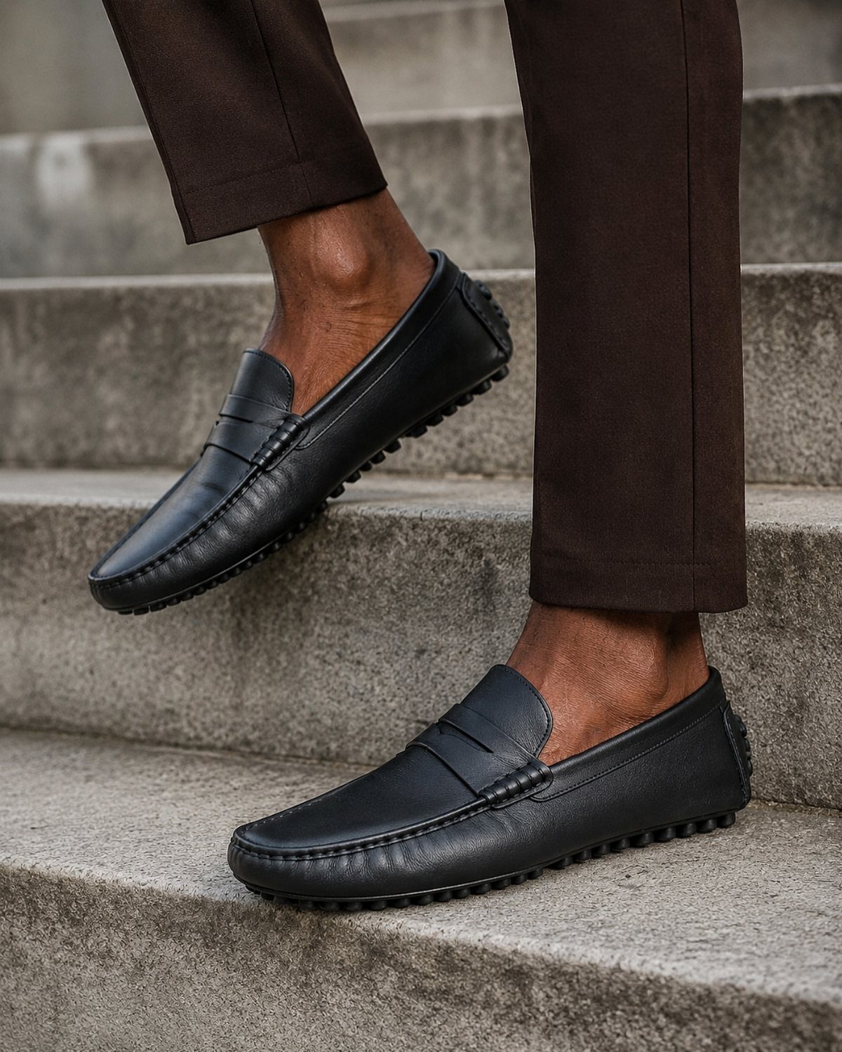 Black leather loafers worn by a person standing on grey stone stairs.