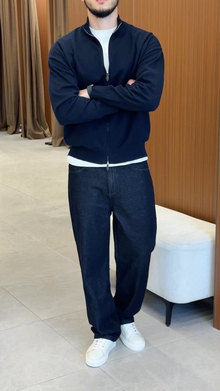 Man wearing a navy zip-up jacket, white t-shirt, dark jeans, and white sneakers.