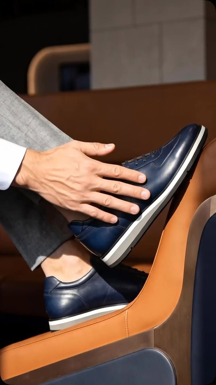 Navy blue leather sneakers worn with grey trousers and a white shirt cuff.