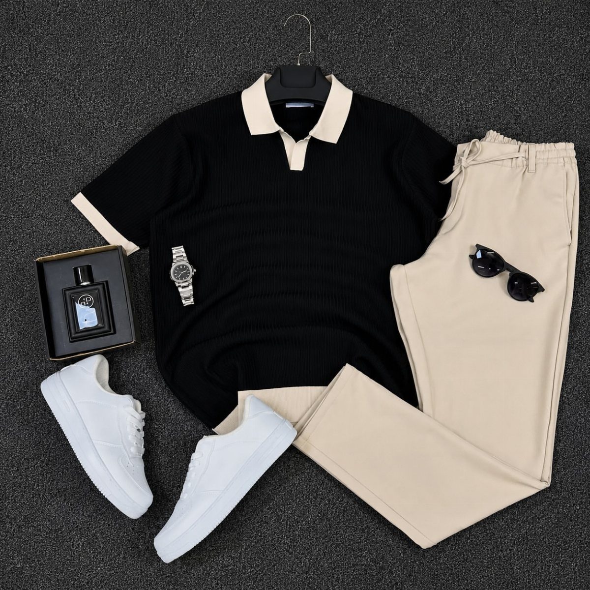 Black polo shirt, cream trousers, white sneakers, sunglasses, and accessories arranged in a flat lay.