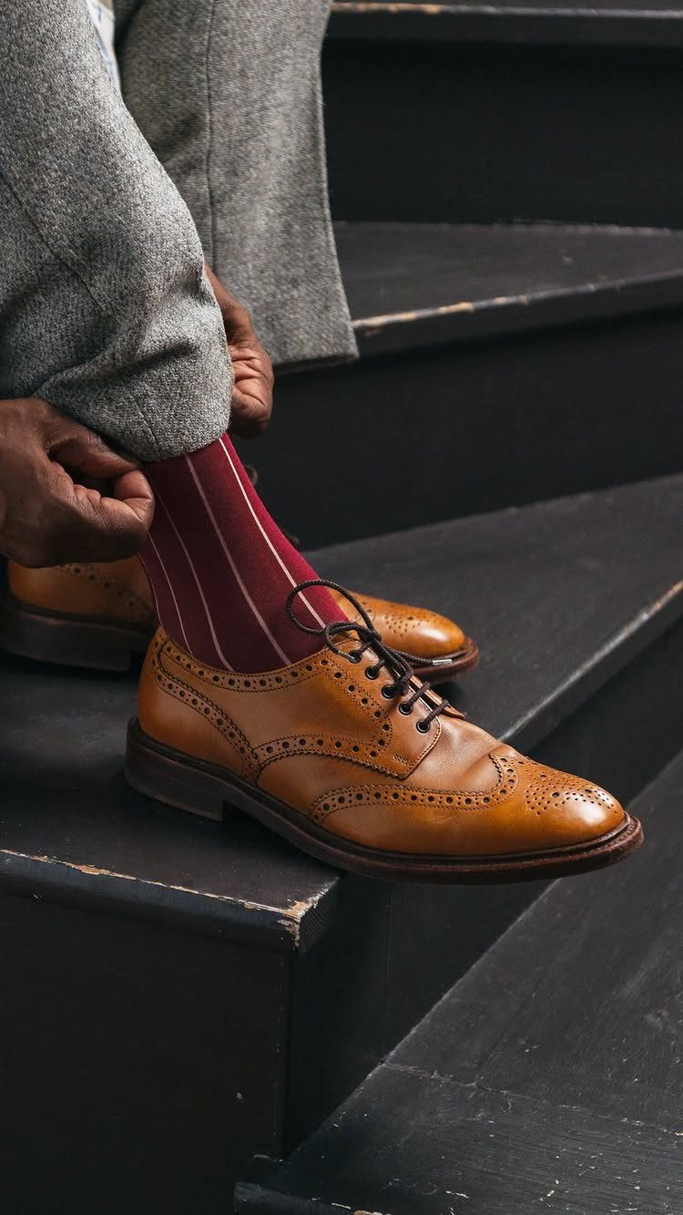 Tan leather brogue shoes worn with burgundy striped socks on black stairs.