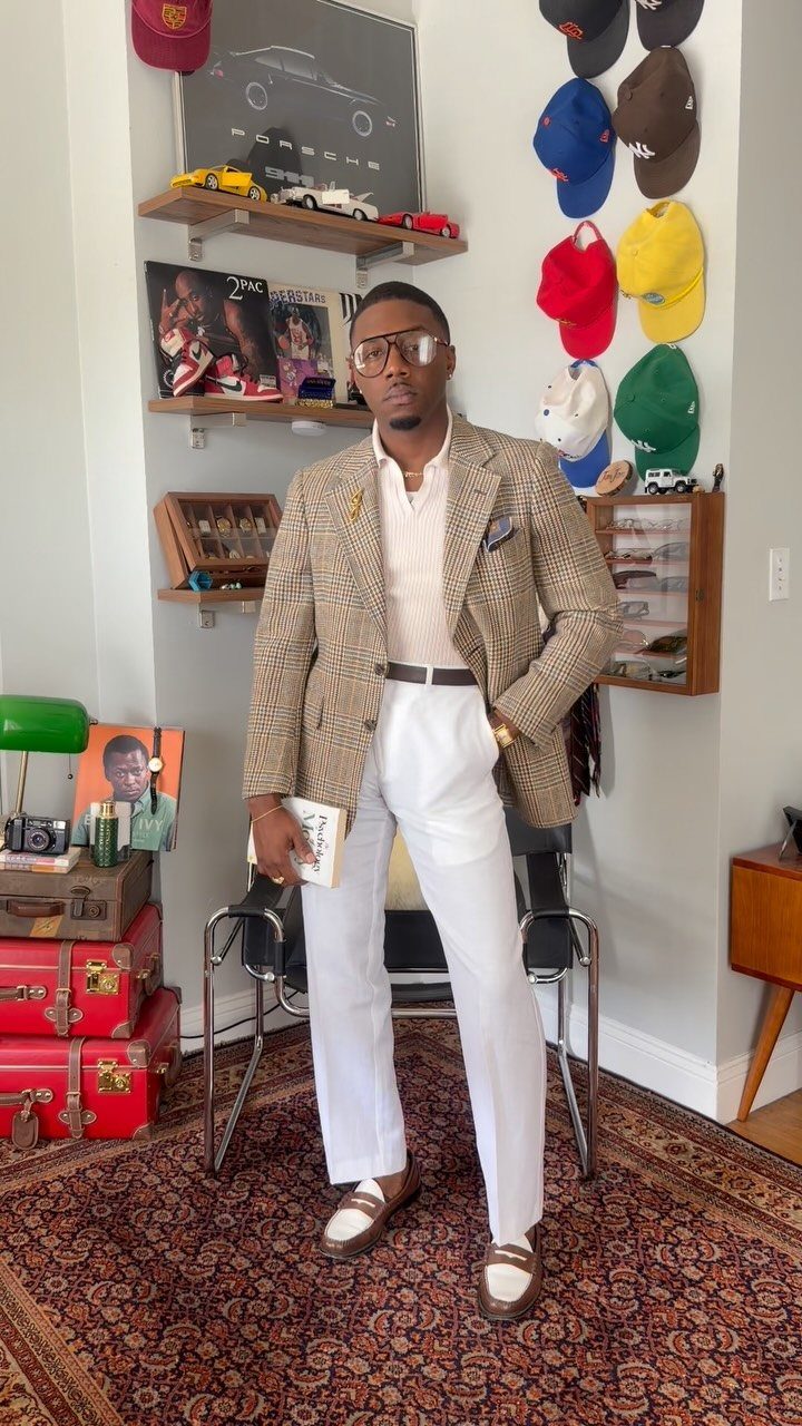 Man wearing a patterned sport coat, white trousers, and brown leather loafers standing in a room.