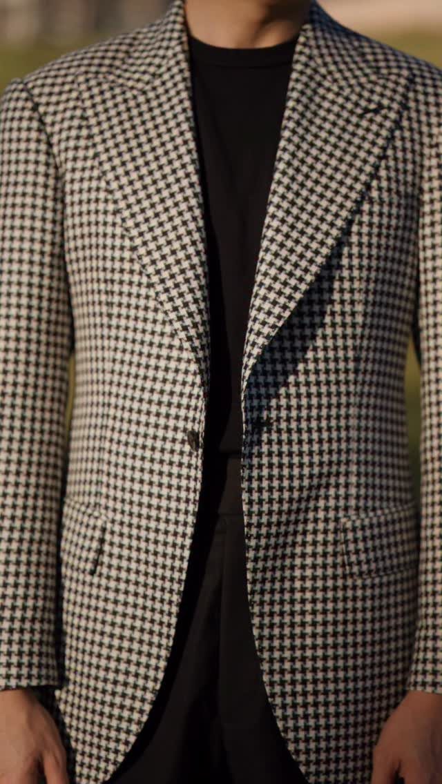 A person wearing a black and white houndstooth patterned sport coat over a black t-shirt.