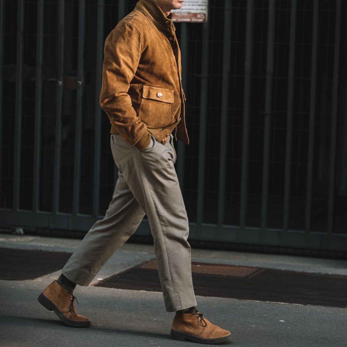 A man walking in a tan suede jacket, beige trousers, and brown boots.