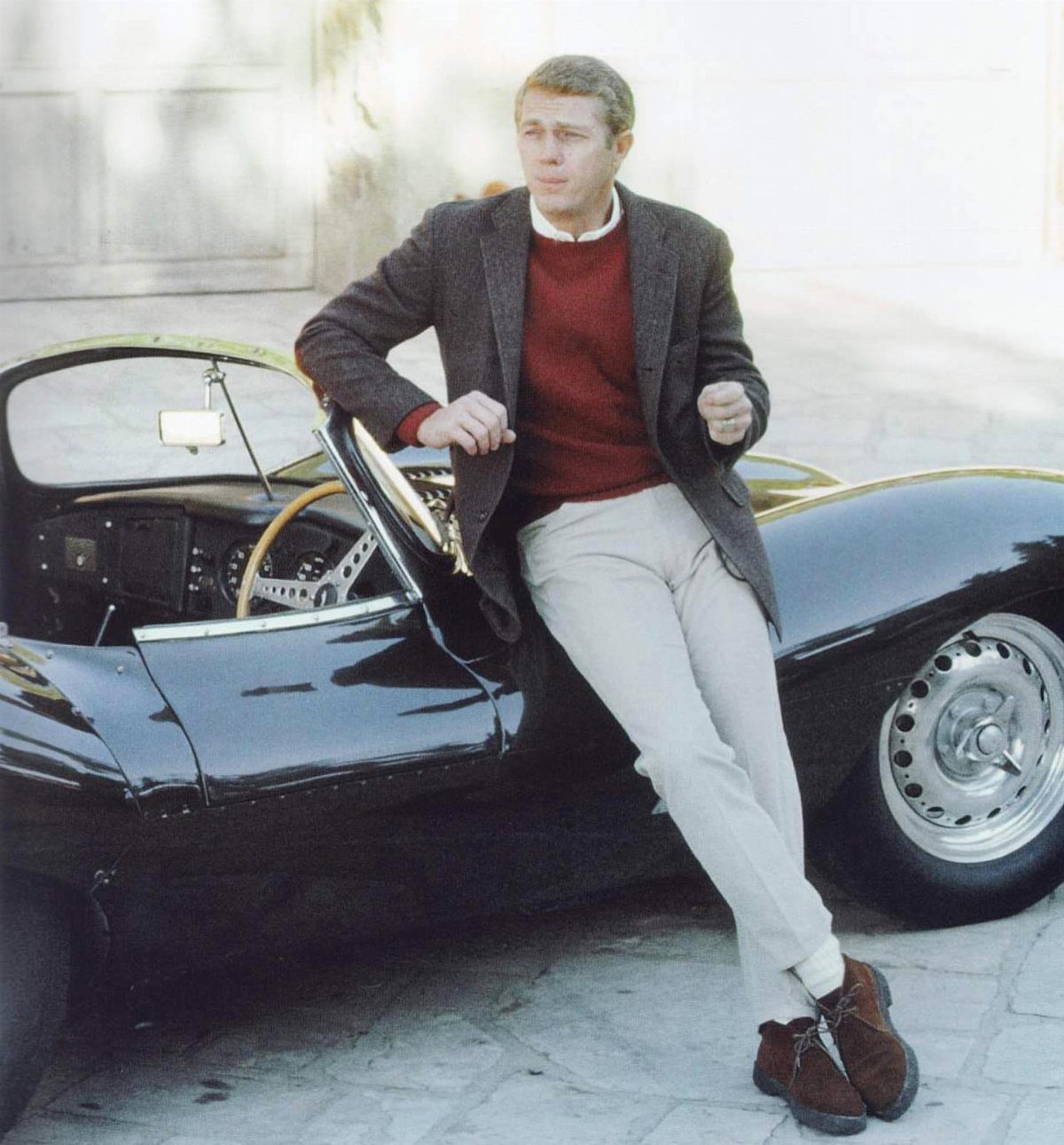 Man wearing a tweed sportcoat and burgundy sweater leaning against a vintage black sports car.