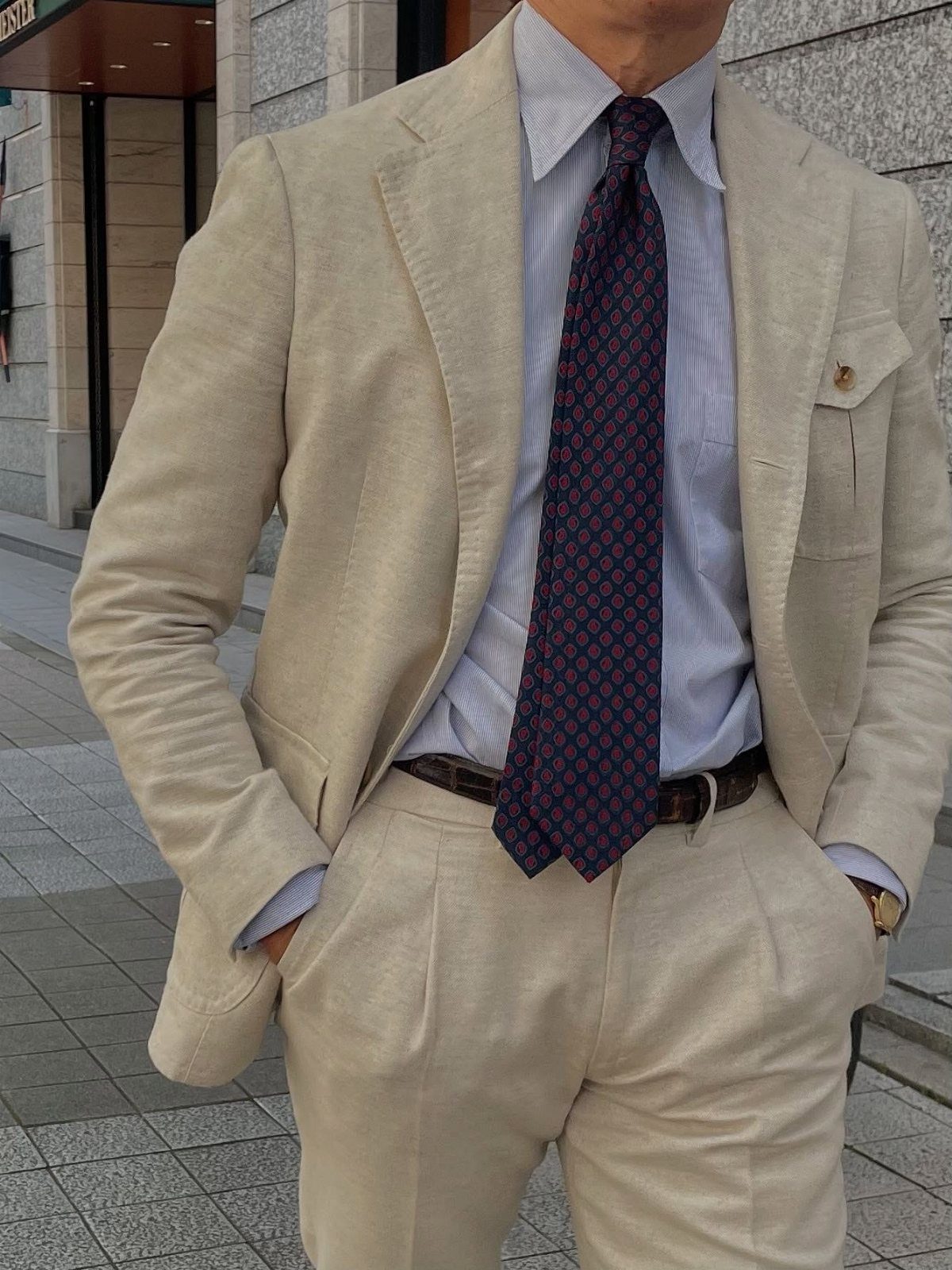 A man wearing a light beige linen suit with a blue striped shirt and patterned tie.