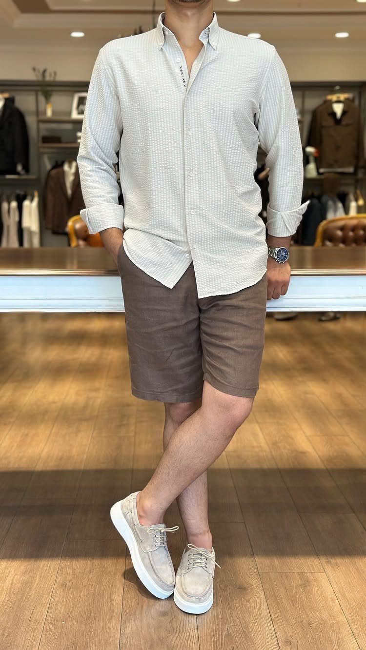 Man posing in a light grey button-down shirt, brown shorts, and beige sneakers.