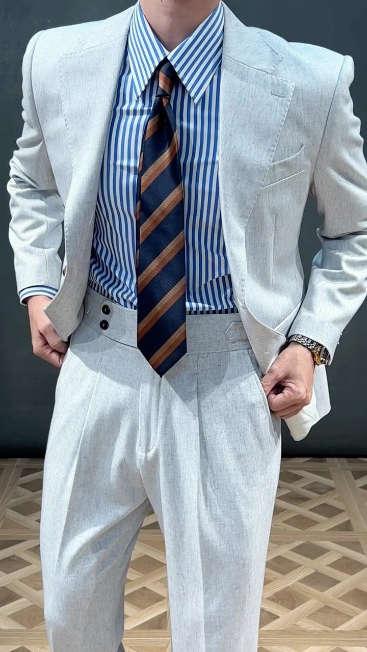 Man wearing a light grey summer suit with a blue striped shirt and a patterned tie.