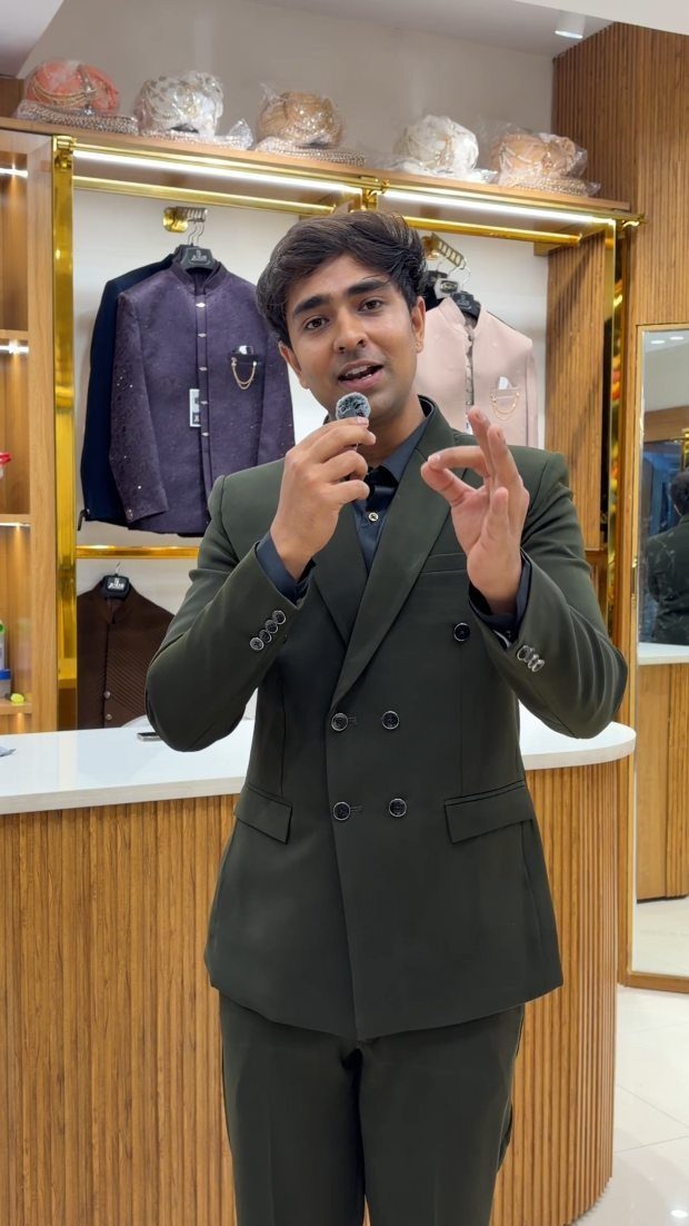 Man in a dark green double-breasted suit speaking into a microphone in a boutique.
