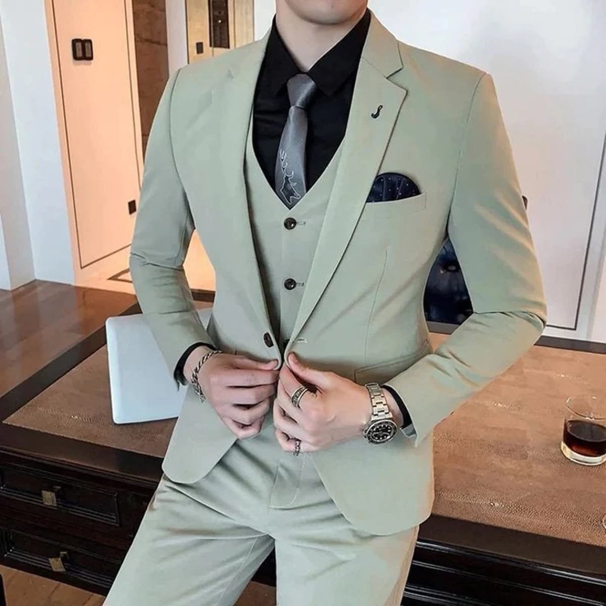 Man posing in a slim fit sage green three-piece suit with a black shirt and grey tie.