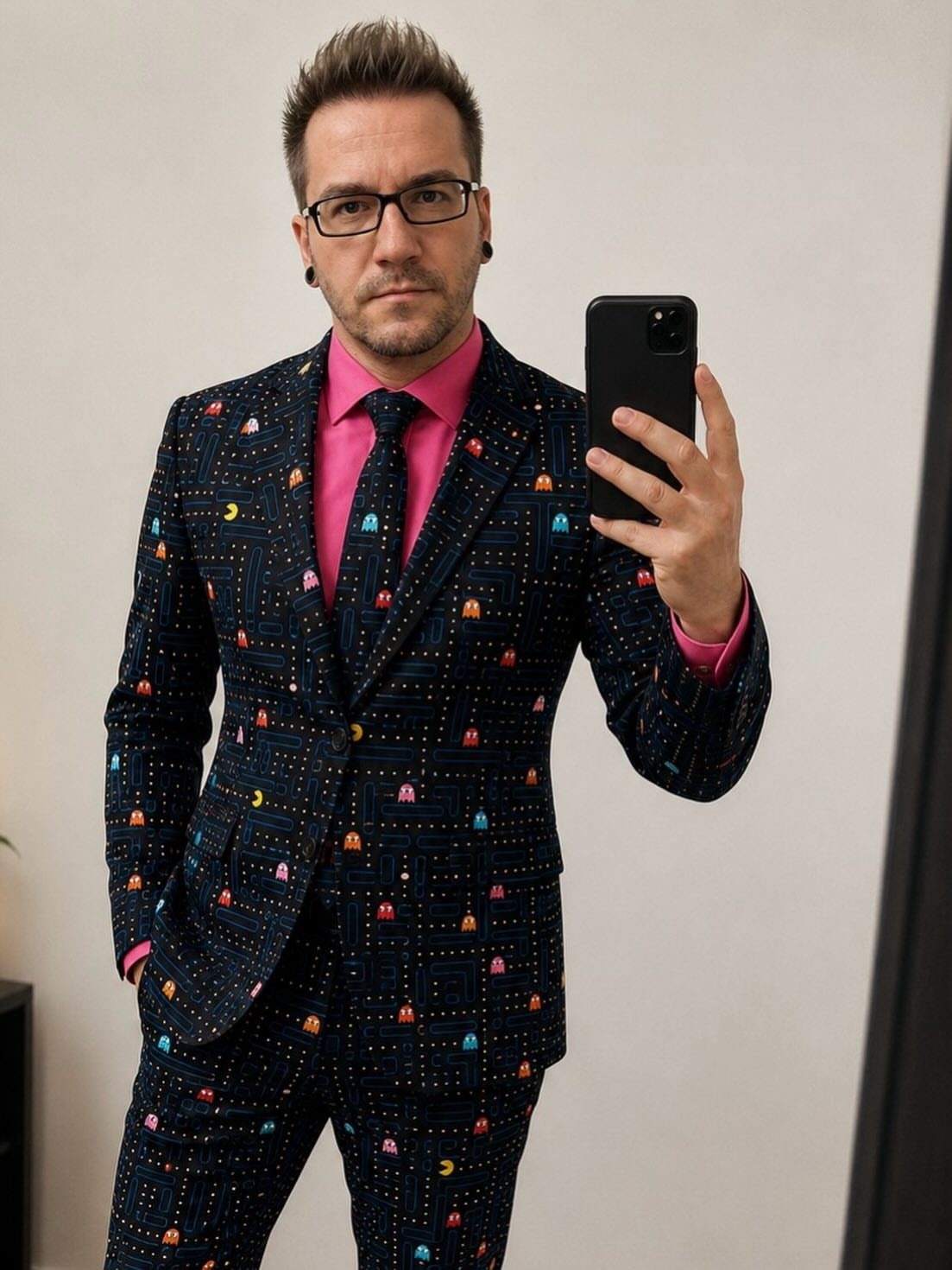 Man in a navy suit featuring colorful Pac-Man game patterns and a pink shirt.