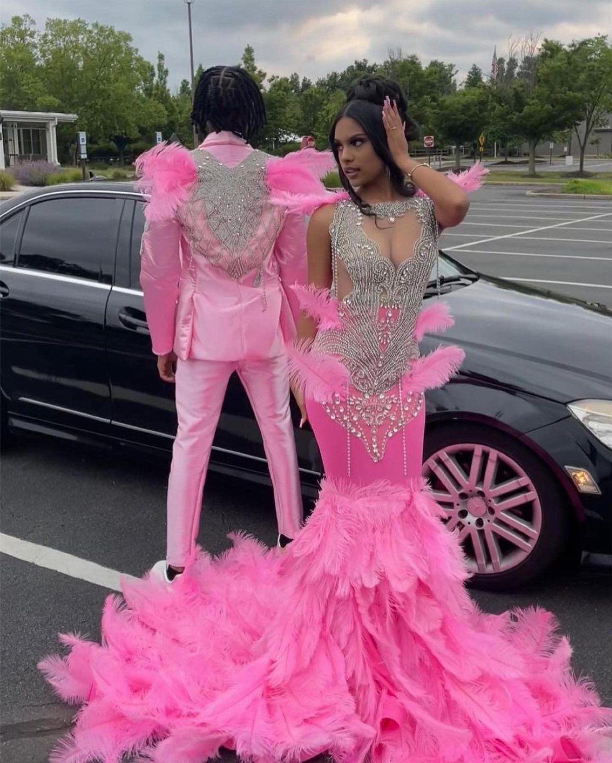 A man in a pink feathered suit and a woman in a pink feathered gown standing by a car.